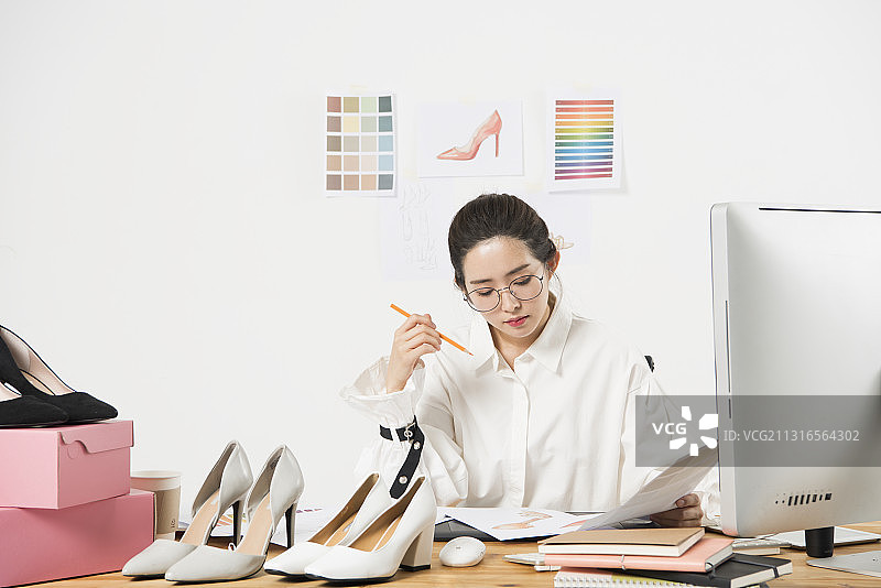拿着铅笔的女人坐在书桌旁，用电脑和笔记本设计鞋子图片素材