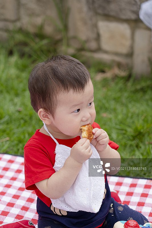 野外草坪垫上快乐吃东西的女婴图片素材