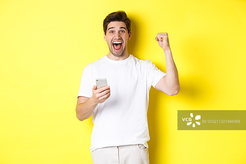 一个微笑的男人站在黄色背景下使用手机的肖像图片素材