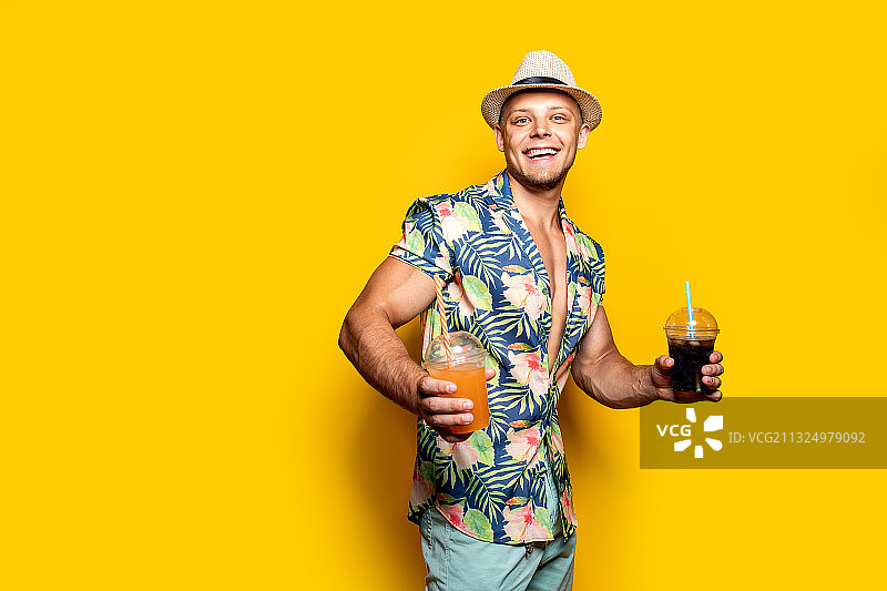 一个微笑的男人拿着饮料，站在黄色的背景下图片素材