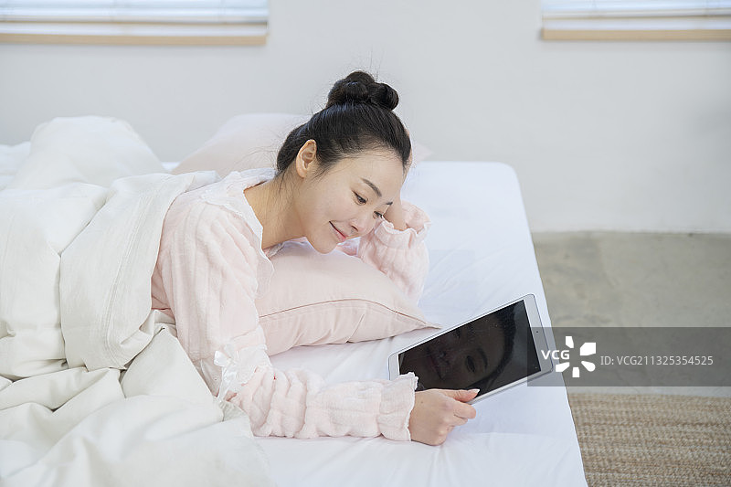 亚洲女性在床上使用数字平板电脑图片素材