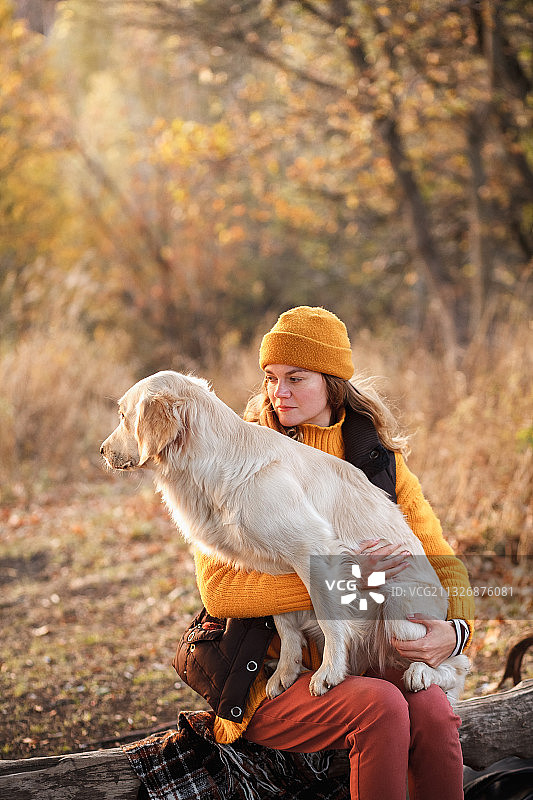 在俄罗斯的森林里，穿着黄色衣服的女人和一只金毛猎犬在一起图片素材