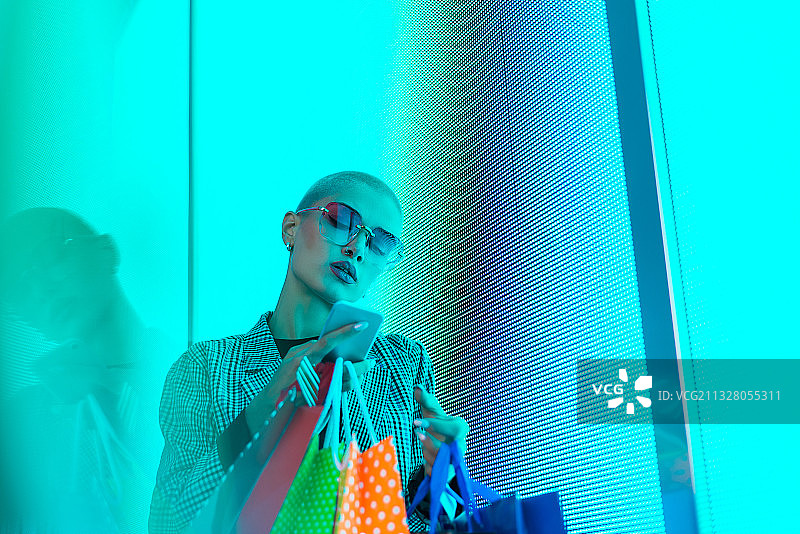 美丽的年轻女子站在购物袋对照明LED灯在晚上图片素材