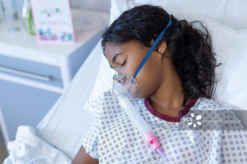 生病的混血女孩戴着氧气面罩睡在医院的病床上图片素材