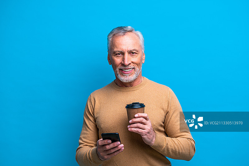 一个微笑的男人拿着手机，站在蓝色背景下图片素材