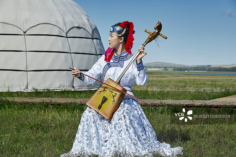 草原上蒙古包前穿着蒙古族传统服饰演奏马头琴的少女图片素材
