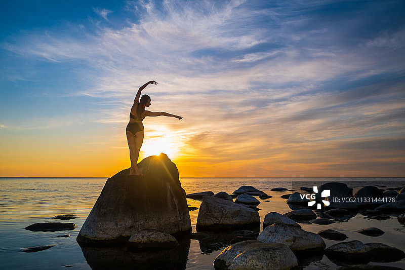 日落时，女人站在岩石上的剪影图片素材