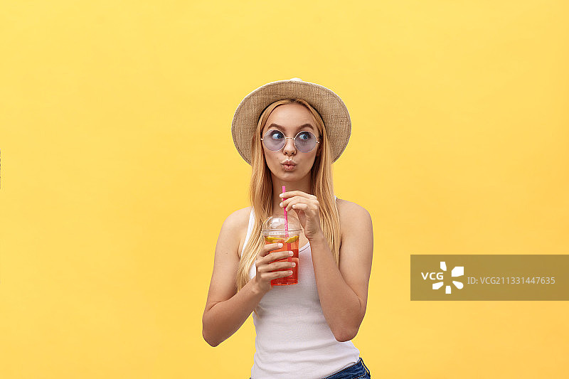 年轻女子喝果汁的肖像，而站在黄色背景图片素材