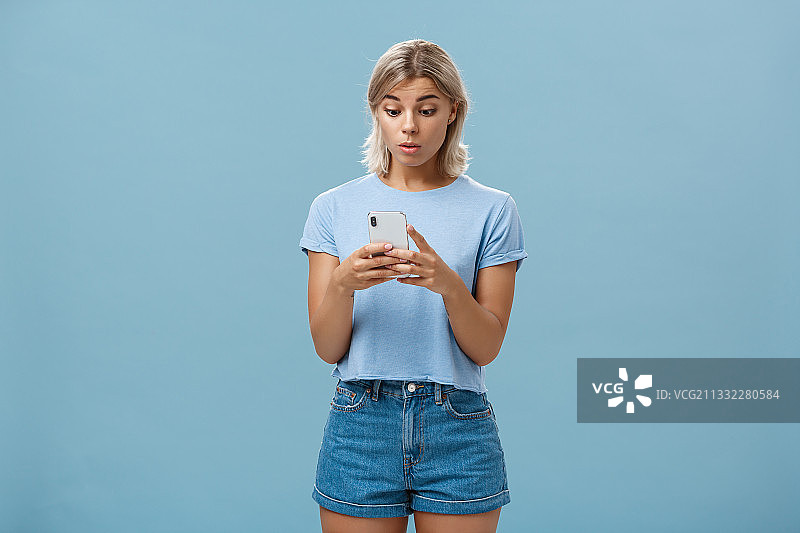 一名年轻女子站在蓝色背景下使用手机图片素材