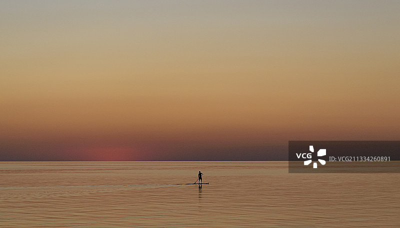 日落时分，年轻人站在立桨板上图片素材