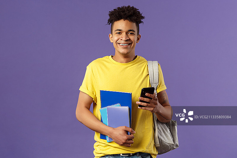 紫色背景下，一名年轻男子拿着智能手机微笑着图片素材