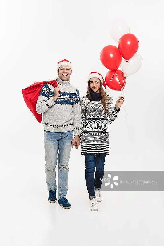 一对情侣穿着圣诞服装，拿着购物袋，站在白色背景下图片素材