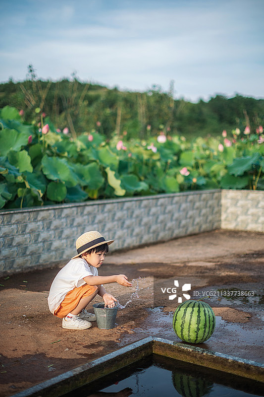 夏天水井旁玩水洗西瓜的男孩图片素材