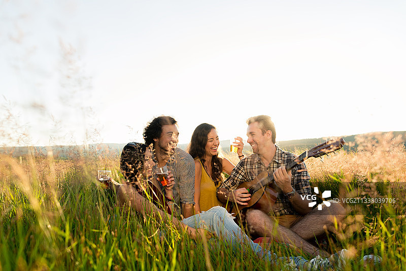 朋友们坐在一起，在草地上弹吉他，不寒而栗图片素材