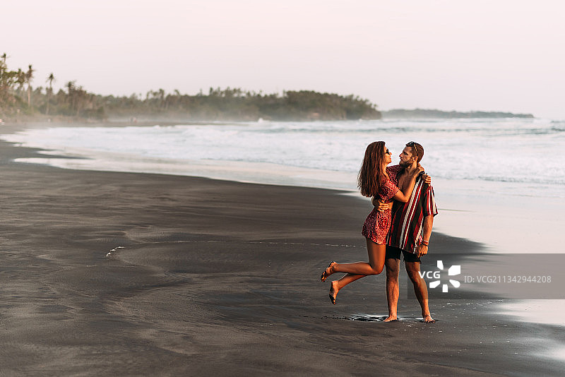 日落时分，一对幸福的情侣沿着海滩散步图片素材