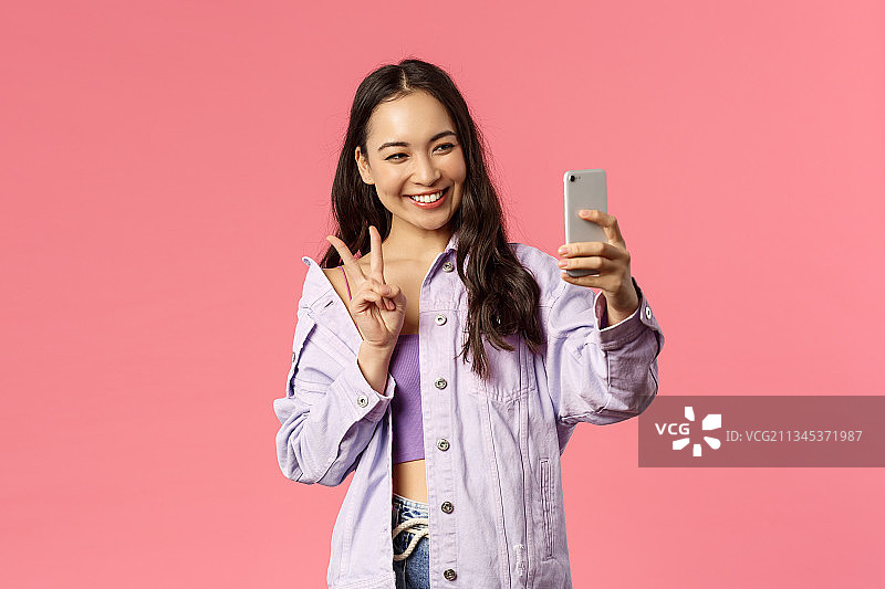 一名微笑的女子手持手机，站在粉红色的背景下图片素材