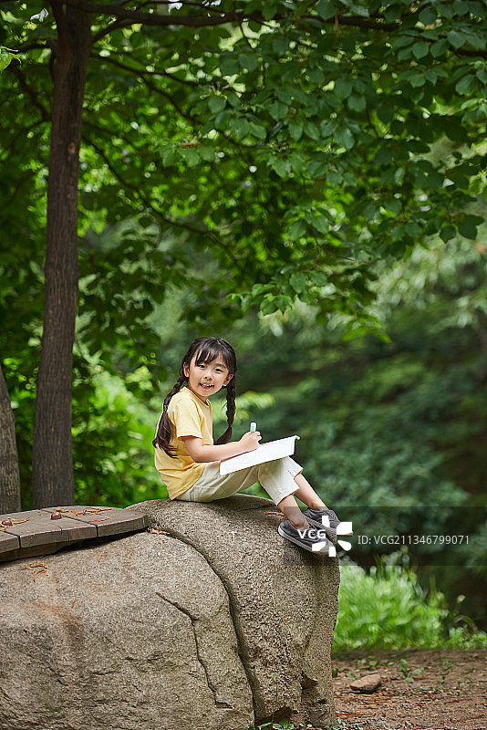 女孩坐在森林里的岩石上，在画板上画画图片素材