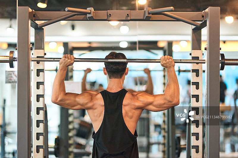 肌肉男在健身房举起杠铃的后视图图片素材