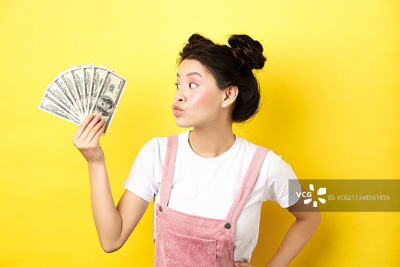 年轻女子手持纸币，站在黄色背景下图片素材