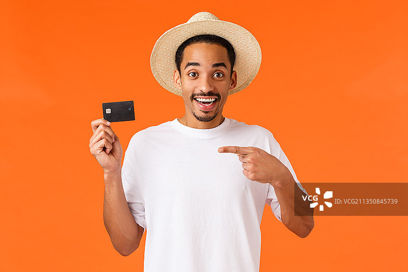 微笑的年轻人的肖像，拿着空白的卡片，站在橙色的背景图片素材
