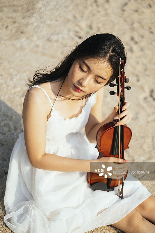 黑色长发的小提琴手坐在沙滩上，用小提琴拉着她的屁股，合上她的eY。图片素材