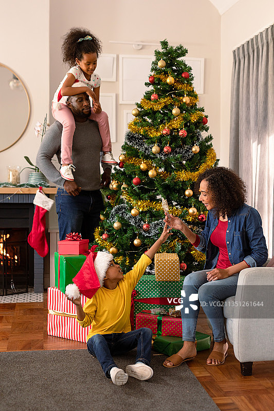 快乐的非洲裔美国父亲戴着圣诞老人的帽子和女儿装饰圣诞树图片素材
