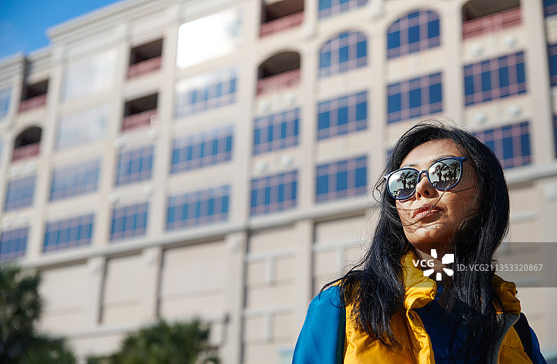 黑发女子，身穿黄色无袖上衣和蓝色衬衫，站在公共建筑的对面图片素材