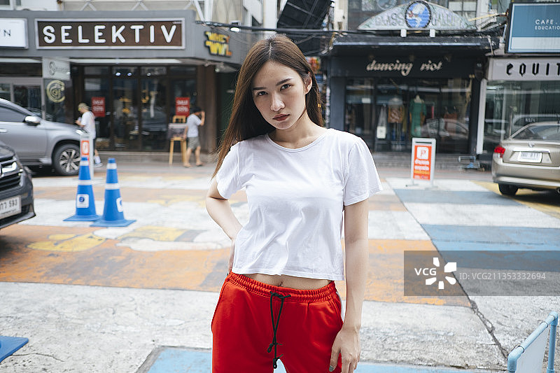 时尚肖像-年轻的亚洲泰国妇女在白色衬衫和红色运动裤站在人行道上。图片素材