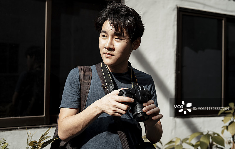 年轻英俊的亚洲摄影师拿着相机准备拍摄。图片素材