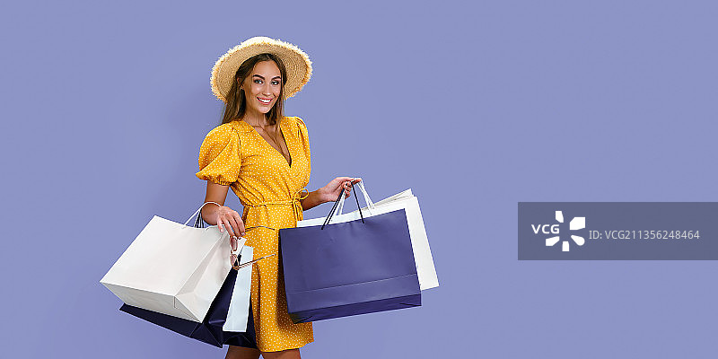 一个带着购物袋微笑的女人的肖像站在紫色的背景下图片素材