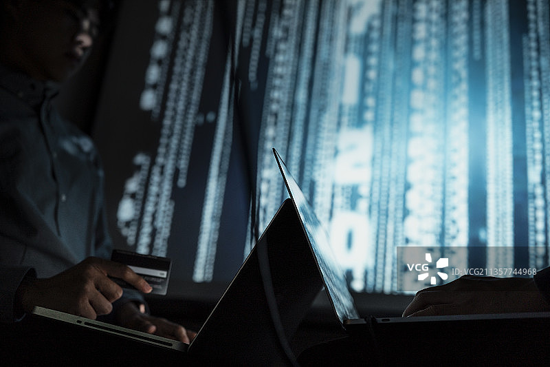 两名黑客在数据库暗服务器室内利用信用卡和笔记本电脑入侵银行，以获取资金。图片素材