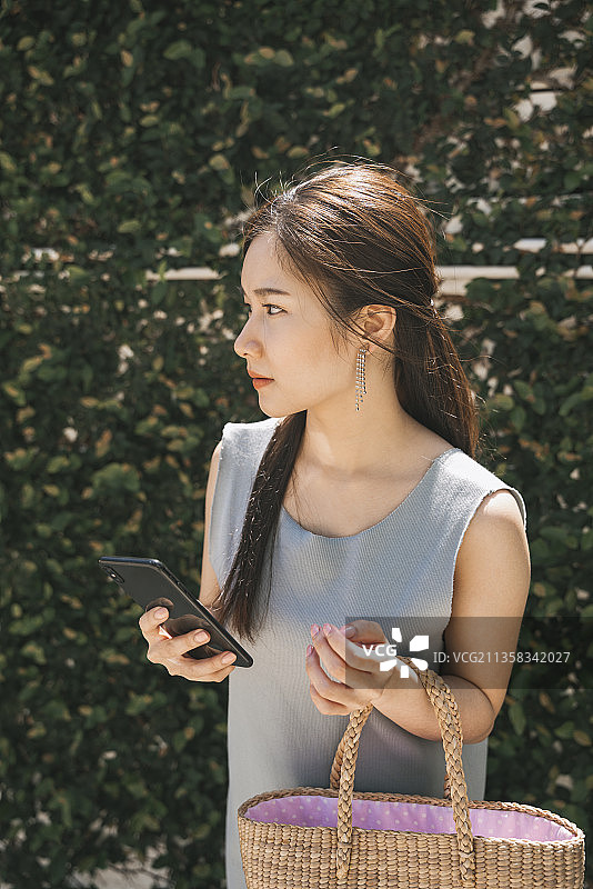 侧视-年轻的亚洲美女手持智能手机和购物。房子的妻子的概念。图片素材