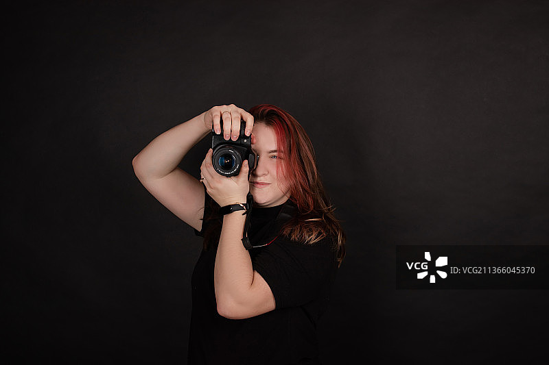 红发女孩与专业相机摆姿势在黑色背景图片素材