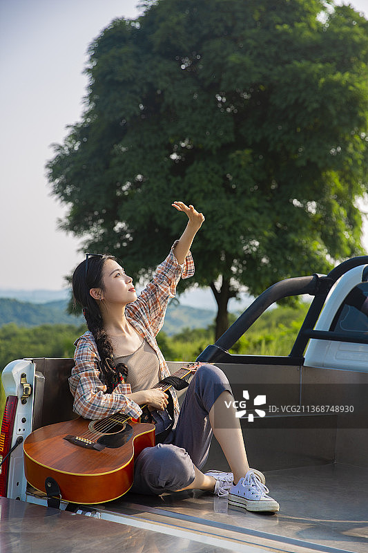 年轻女子户外旅行坐在皮卡车里拿着吉他图片素材