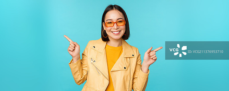 快乐时尚的中国女孩戴着太阳镜，手指指向一边图片素材