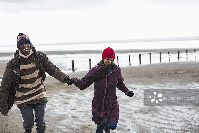 幸福无忧无虑的夫妇牵着手，在潮湿的冬季海滩上奔跑图片素材
