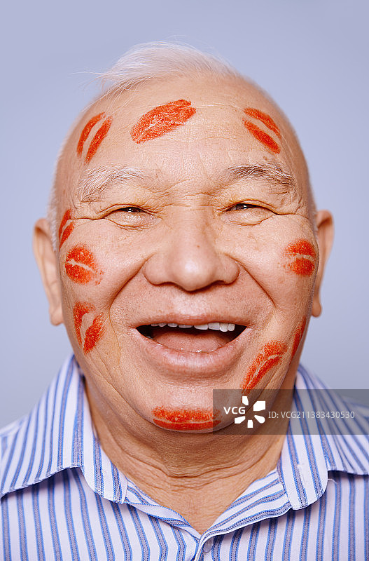 工作室拍摄的无忧无虑和顽皮的年长男子脸上覆盖着口红吻图片素材