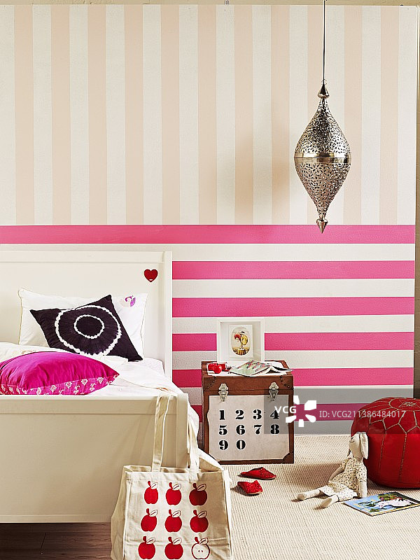 在女孩的卧室里，乡村风格的床和柜子后面的墙壁上有粉红横条纹和淡粉色竖条纹作为床头柜图片素材