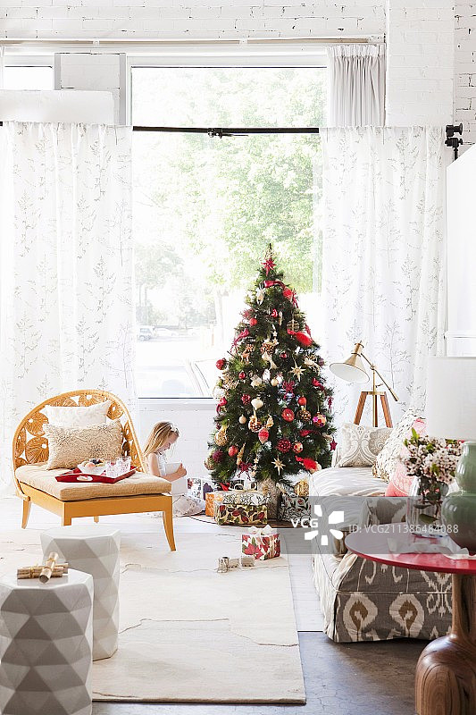 客厅有扶手椅和沙发;小女孩坐在圣诞树旁，背景是成堆的礼物图片素材