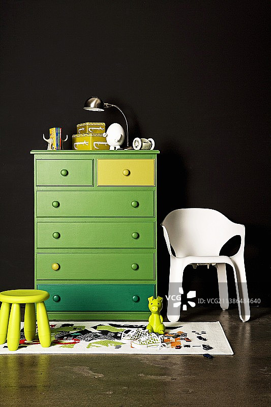 黑色墙壁上的绿色抽屉柜;旁边是一张白色的塑料椅子和一张儿童凳子图片素材