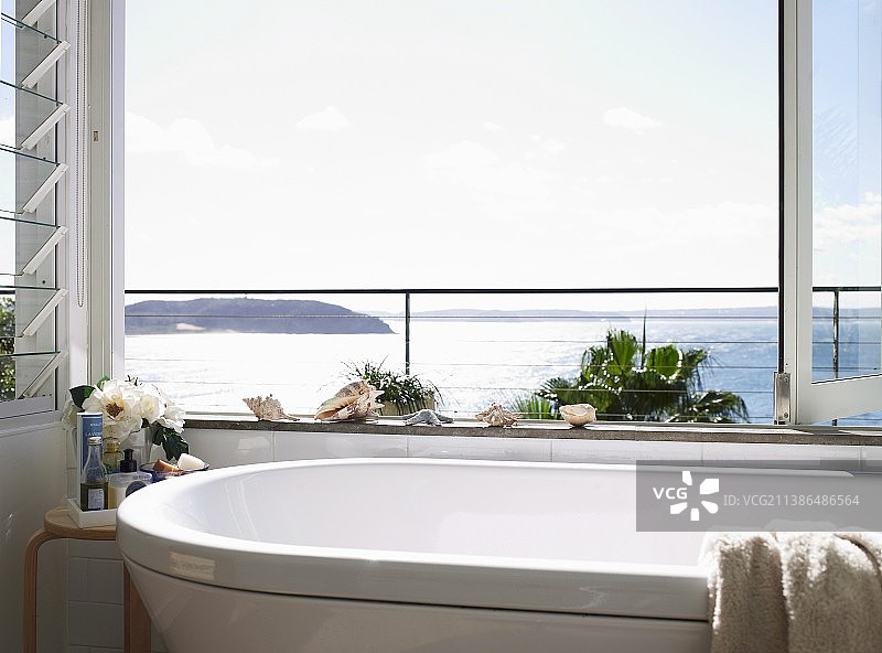 浴室通过开放式折叠玻璃窗可以看到壮丽的海景;浴缸边缘的贝壳装饰图片素材