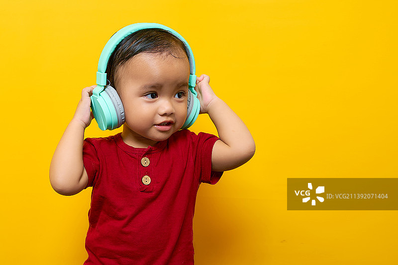 欢快的亚洲小男孩，2岁的小男孩，印度尼西亚，戴着耳机听着最喜欢的音乐图片素材