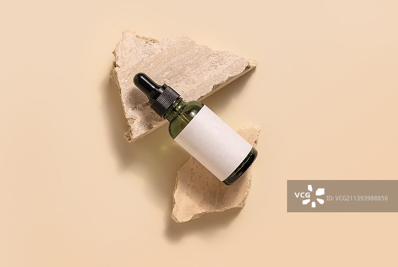 绿色玻璃滴管瓶与空白标签躺在米色石头上黄色化妆品模型图片素材
