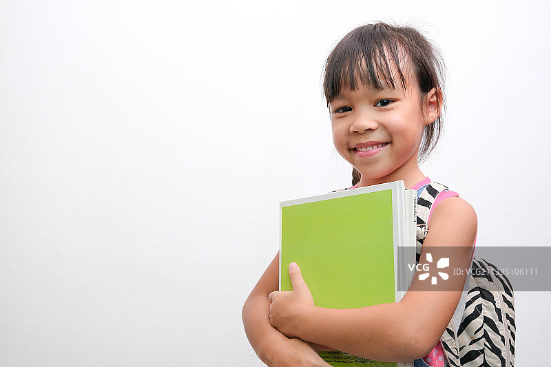 回到学校微笑的小女孩背着书包拿着书看，泰国图片素材