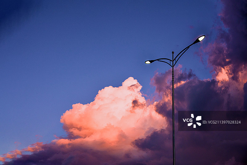 傍晚的路灯亮起，一朵积雨云也被太阳照亮图片素材