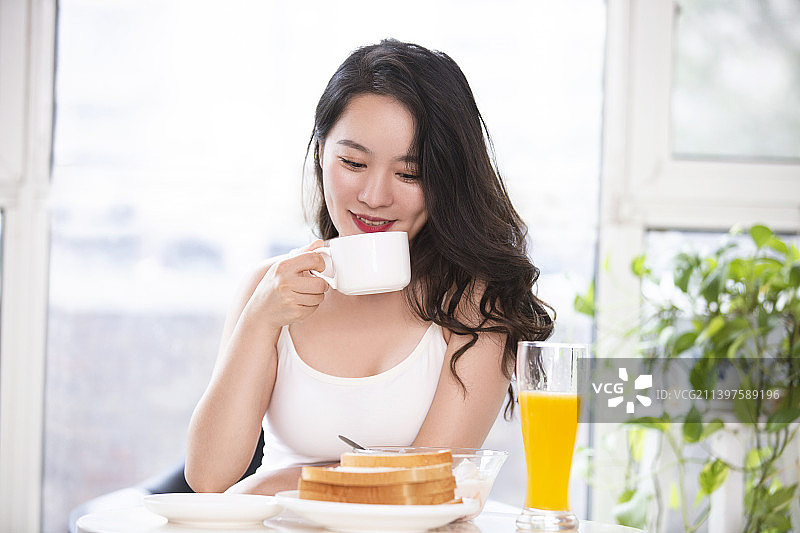 漂亮的年轻女子在家吃早餐喝咖啡图片素材