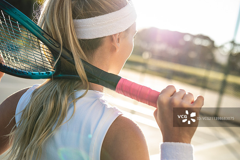 年轻的金发白人女网球运动员的后视图与球拍绕在脖子上的法庭图片素材