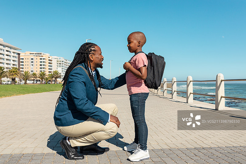非裔美国父亲在散步时蹲着和儿子说话，手放在肩膀上图片素材