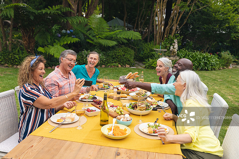 多种族的老年朋友在后院聚会上一边吃饭一边看智能手机图片素材