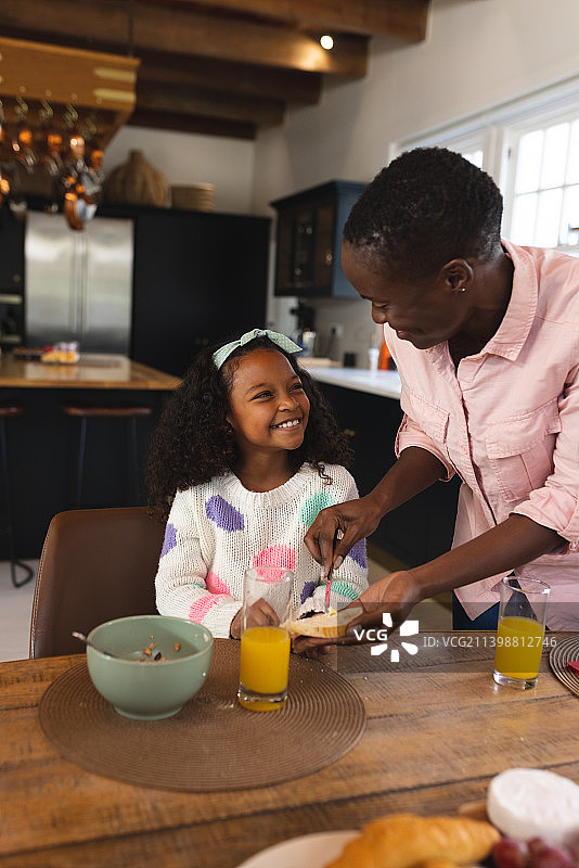 快乐的非裔美国女孩和妈妈一起吃早餐的垂直图像图片素材